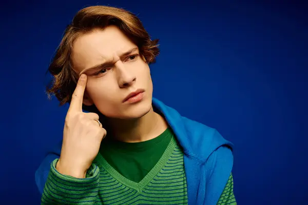 A stylish young man poses thoughtfully against a bold blue background, exuding flair. — Stock Photo