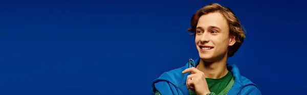 In a vibrant blue setting, a stylish young man smiles confidently in modern attire. — Stock Photo