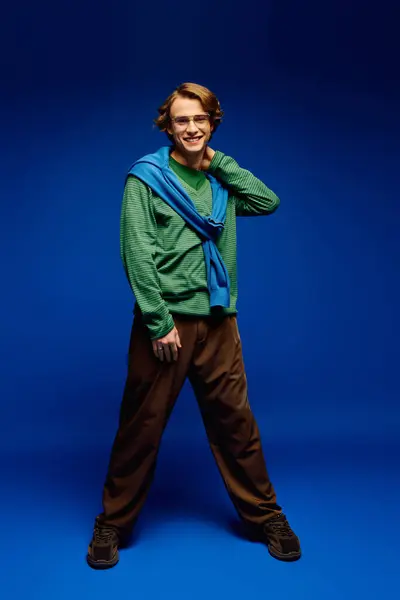 This trendy young man showcases contemporary fashion in a vibrant blue backdrop, exuding charm. — Stock Photo