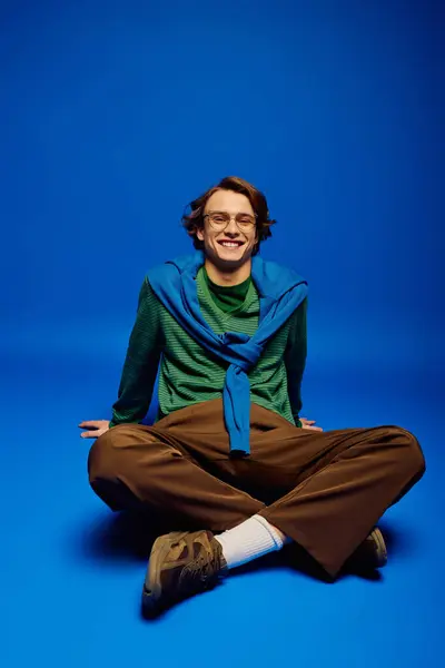 A young man sits comfortably on the floor, dressed in stylish attire, exuding a trendy vibe. — Stock Photo