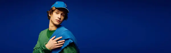 Stylish young man shows off modern attire with charisma against a vibrant blue backdrop. — Stock Photo