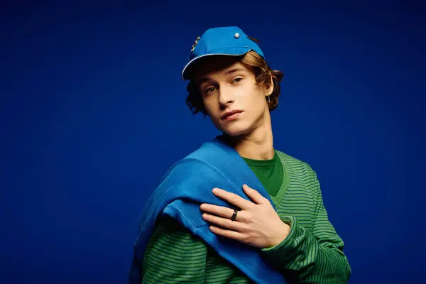 The young man confidently poses in a trendy outfit with a blue sweater over his shoulder. — Stock Photo