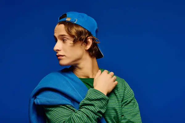 Young man showcases trendy attire and a stylish hat in a colorful, creative setting. — Stock Photo