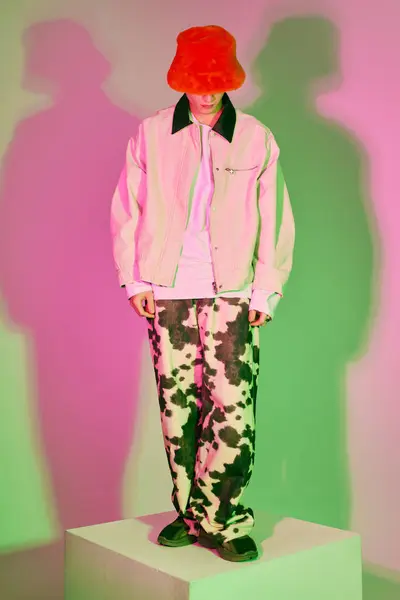 Confident young man on a pedestal flaunts bold fashion against vibrant backgrounds. — Stock Photo
