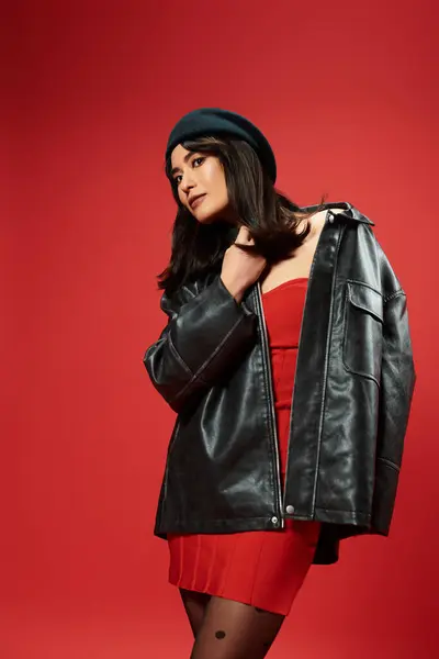 Young asian woman exudes style in a striking red dress and leather jacket against a bold backdrop. — Stock Photo