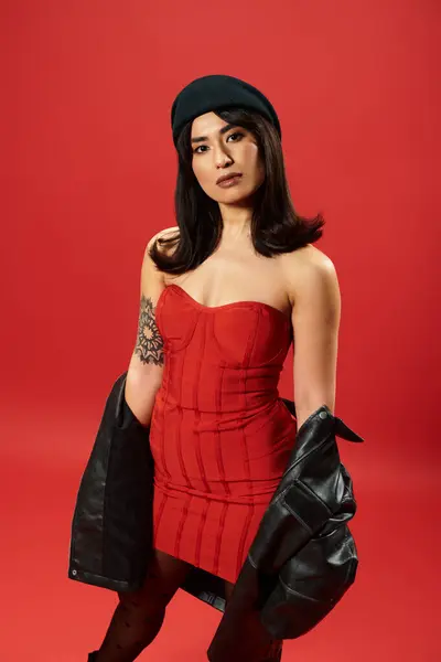 A confident young asian woman poses elegantly in a striking red dress, exuding a trendy vibe. — Stock Photo