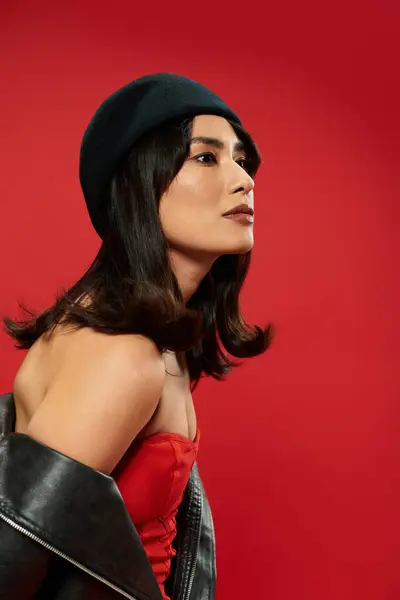 A stylish young Asian woman shows off her trendy outfit against a bold red background. — Stock Photo