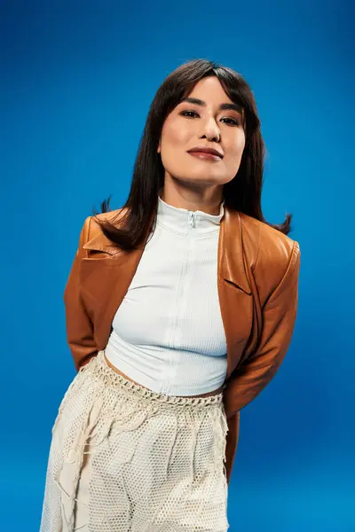Confident young Asian woman poses in stylish attire against a vibrant blue background. — Stock Photo