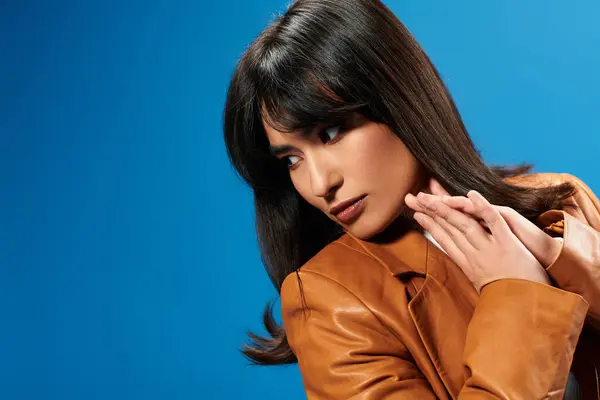Una joven asiática confiada exhibe la moda moderna contra un audaz telón de fondo azul. - foto de stock