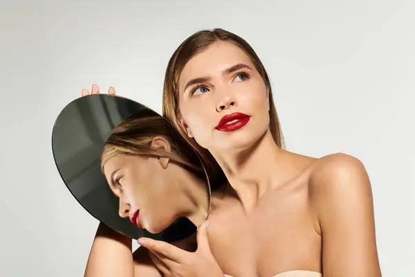 Una giovane donna elegante con un'espressione fiduciosa guarda il suo riflesso in uno specchio rotondo. — Foto stock