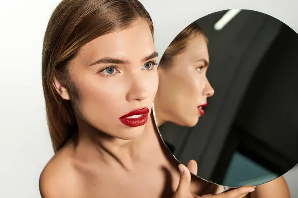 Una giovane donna ammira il suo riflesso, trasudando fiducia ed eleganza in uno spazio elegante. — Foto stock
