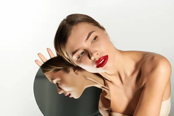 Una giovane donna posa con uno specchio, mostrando le sue caratteristiche sorprendenti e il rossetto audace. — Foto stock