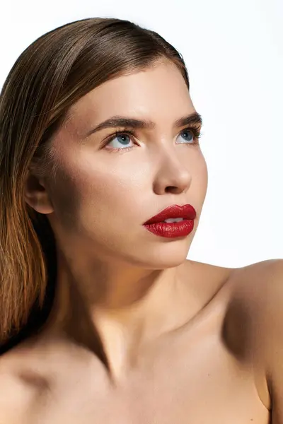 A young woman highlights her beauty with bold red lips and radiant skin in soft lighting. — Stock Photo