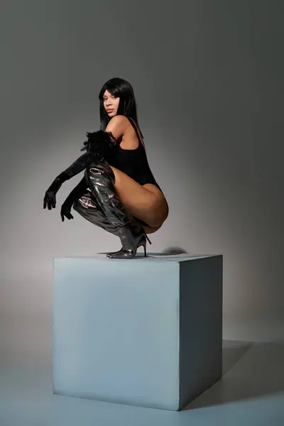 In einem modernen Atelier zeigt eine stilvolle Frau ihren einzigartigen Sinn für Mode, während sie auf einem Würfel posiert. — Stockfoto
