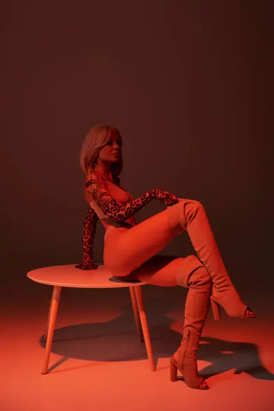 Young woman with intricate tattoos poses confidently on a round table in striking red hues — Stock Photo