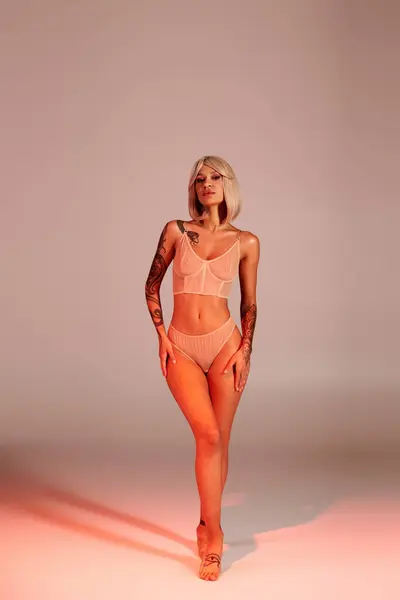 Stylish woman with tattoos poses confidently in a chic ensemble against a minimal backdrop. — Stock Photo