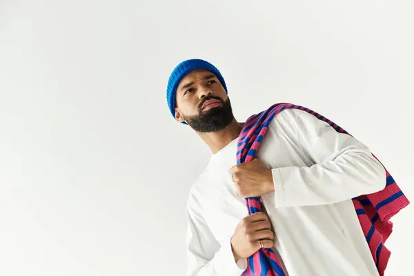 A confident man displays modern style with a bright beanie and stylish scarf in a chic place. — Stock Photo
