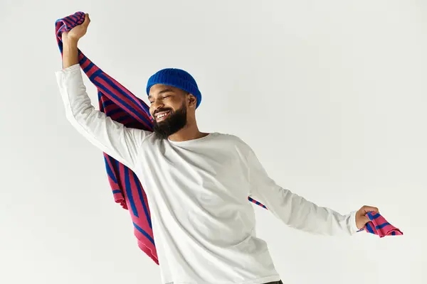 A stylish young man beams with joy, playfully holding a colorful scarf in a bright setting. — Stock Photo