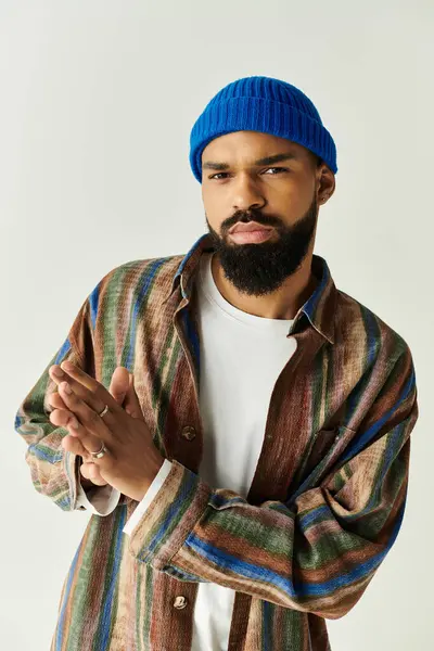 Un jeune homme confiant dans une chemise rayée colorée et un bonnet bleu rayonne de style et de charme. — Photo de stock