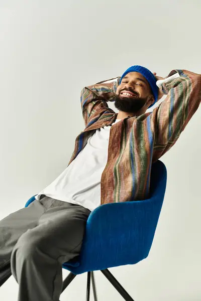 Handsome man wearing a colorful shirt relaxes in a blue chair while smiling broadly. — Stock Photo