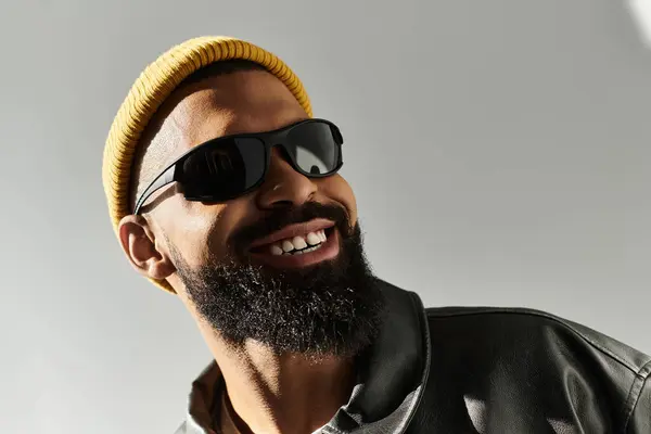 Charming young man with a beard smiles confidently while wearing sunglasses and a yellow beanie. — Stock Photo