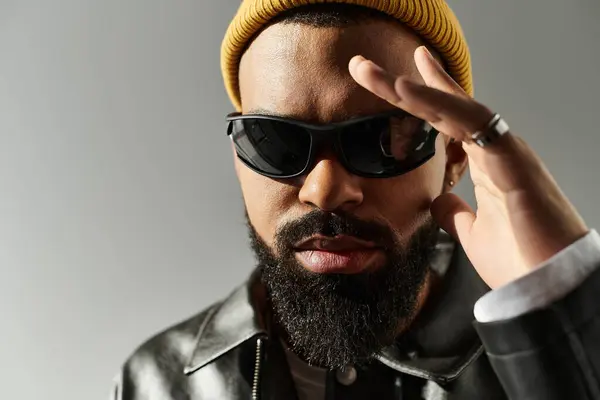 Handsome man sports sunglasses and a beanie while posing stylishly against a gray backdrop. — Stock Photo