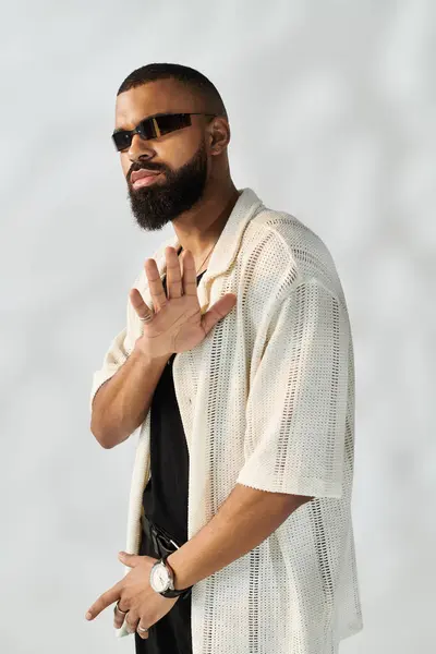 Joven con barba muestra su atuendo de moda y gafas de sol mientras posa con confianza. - foto de stock