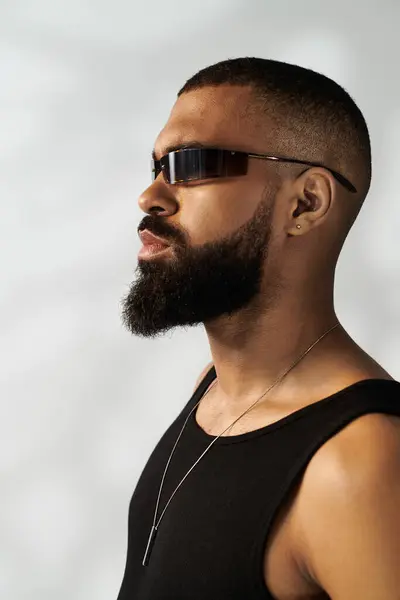 Ein stylischer junger Mann in schwarzem Tank-Top und Sonnenbrille posiert selbstbewusst im hellen Sonnenlicht. — Stockfoto