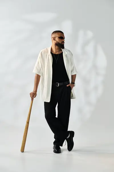 A stylish young man confidently holds a wooden bat in a trendy setting. — Stock Photo