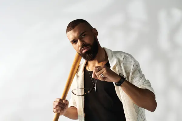 Young man exudes confidence and style indoors, clutching a baseball bat and sunglasses in hand. — Stock Photo