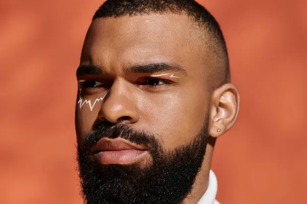 Handsome man exudes confidence with unique facial art against a vibrant background. — Stock Photo