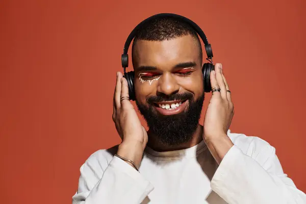 Young man with a fashionable look smiles while wearing headphones, immersed in music vibes. — Stock Photo