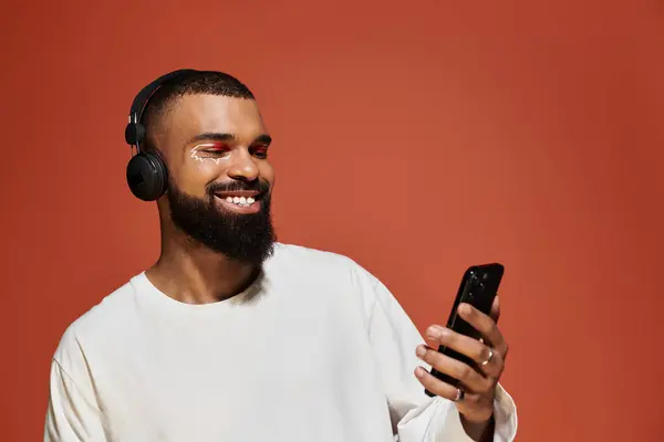 Giovane uomo con le cuffie sorride mentre utilizza il suo smartphone in un ambiente vivace. — Stock Photo