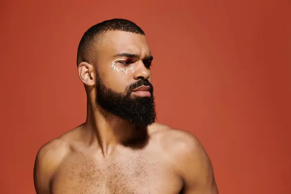 A young man with a well groomed beard poses confidently against a bright orange backdrop. — Stock Photo