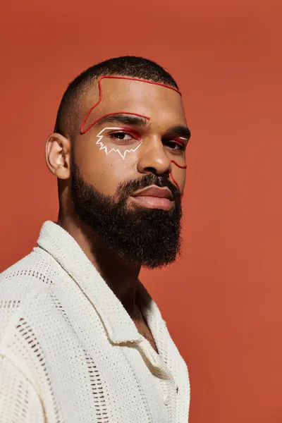 Confident young man showcases striking makeup against a warm toned backdrop. — Stock Photo