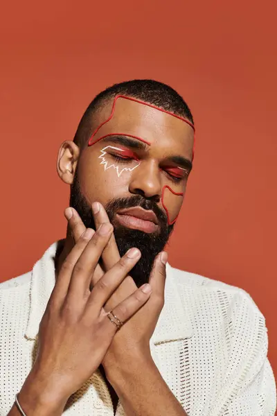 A handsome young man confidently poses with striking facial art in a warm toned setting. — Stock Photo