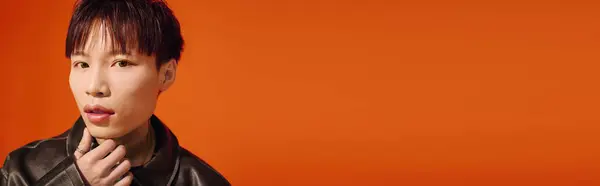 Handsome young man with a fashionable look stands against a warm orange background, exuding charm. — Stock Photo