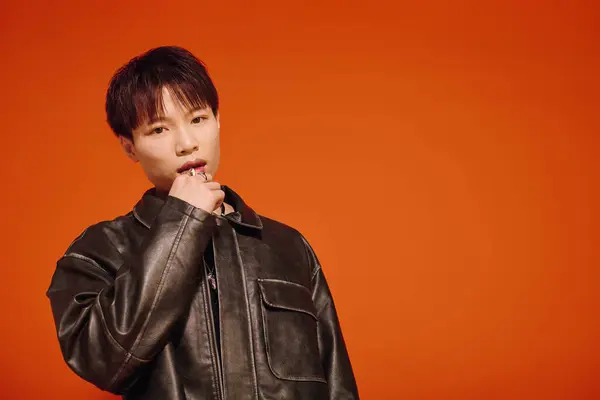 A charming young man in a black leather jacket stands against a bright orange backdrop. — Stock Photo