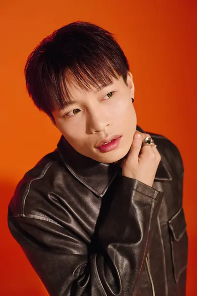 A stylish young Asian man poses strikingly against an orange backdrop. — Stock Photo
