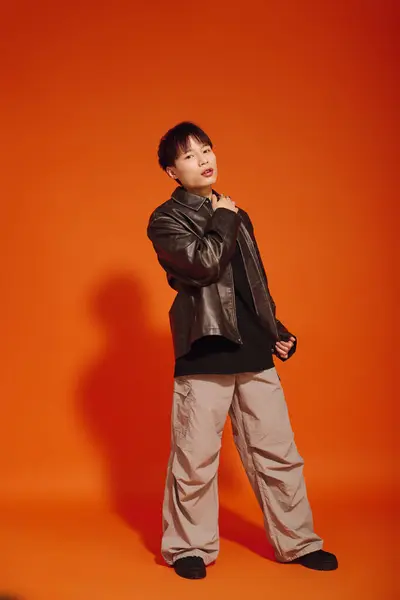 A stylish young Asian man poses confidently against an eye catching orange background. — Stock Photo