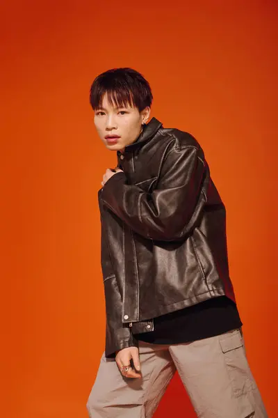 A young Asian man exudes confidence in a stylish outfit against a vivid orange backdrop. — Stock Photo