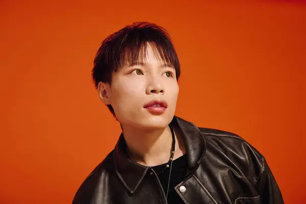 Young man with a trendy outfit is confidently striking a pose against a bold orange background. — Stock Photo