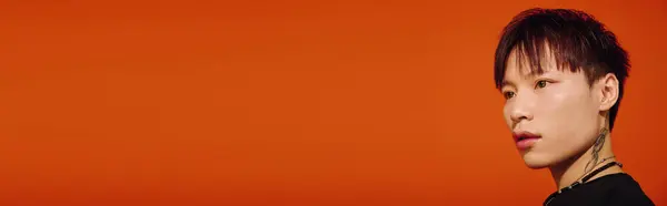 Handsome asian man stands confidently against a bold orange backdrop, showcasing his stylish look. — Stock Photo