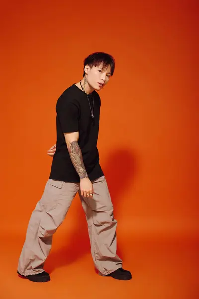 Handsome young man with trendy attire showcases his urban style in a striking orange backdrop. — Stock Photo