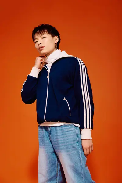 Handsome young man in a trendy outfit stands confidently against a striking orange wall. — Stock Photo