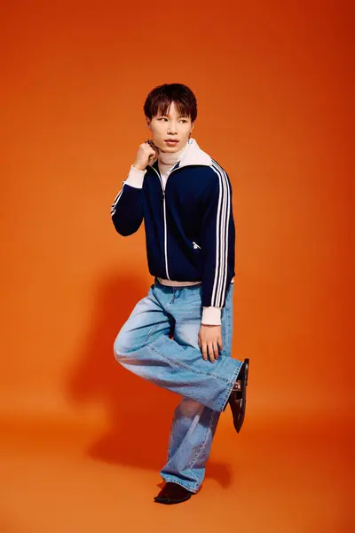 A stylish young Asian man poses with one leg raised against a vibrant orange backdrop. — Stock Photo