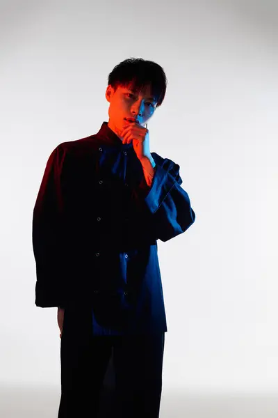 A young Asian man stands thoughtfully, displaying his stylish outfit and vibrant colors. — Stock Photo
