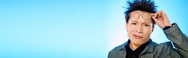 A young Asian man adjusts his glasses, thoughtfully gazing at the camera in stylish attire. — Stock Photo
