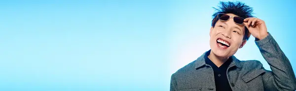 Un giovane, bell'uomo in occhiali da sole sorride ampiamente mentre posa con stile alla luce del sole. — Foto stock