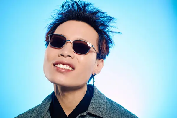 A handsome young man confidently displays his unique style, smiling against a blue backdrop. — Stock Photo